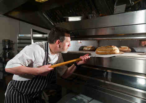 A chef removing a loaf of bread from an oven. 