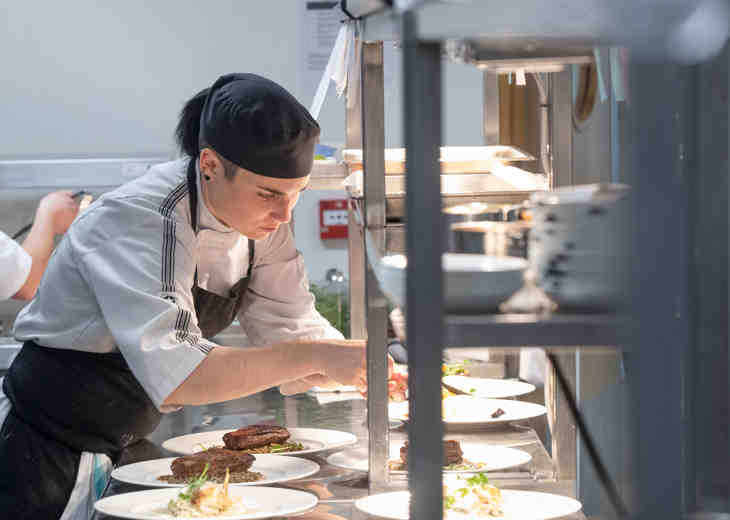 A chef preparing plates of food on a metal kitchen counter.